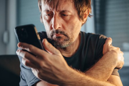 Foto de Hombre leyendo mensaje de texto en el teléfono móvil, hombre descuidado sosteniendo el teléfono celular en el interior, enfoque selectivo - Imagen libre de derechos