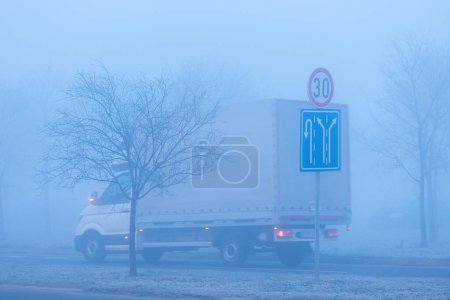 Téléchargez les photos : Trafic dans le brouillard, panneaux routiers et camion sur l'autoroute, mise au point sélective - en image libre de droit