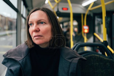 Téléchargez les photos : Contemplative adulte femme caucasienne équitation transport public bus à travers les rues de la ville, accent sélectif - en image libre de droit