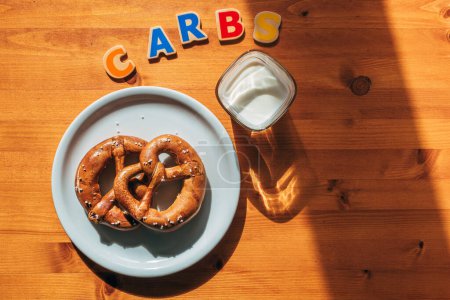Téléchargez les photos : Carbs pour le petit déjeuner concept, verre de yaourt et deux bretzels sur une assiette sur la table le matin, mise au point sélective - en image libre de droit