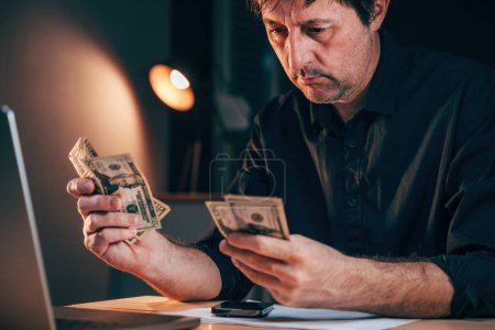 Geschäftsmann, der am Schreibtisch amerikanische Dollars zählt, selektiver Fokus