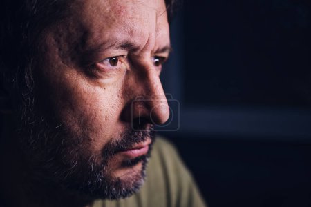Photo for Concerned man, portrait of adult male looking at device screen at night, hearing bad news on television, low key with selective focus - Royalty Free Image