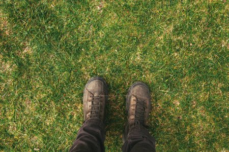 Téléchargez les photos : Vue du dessus des pieds mâles en bottes debout sur pelouse verte avec espace de copie - en image libre de droit