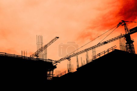 Foto de Construcción y desarrollo de edificios residenciales, grúas retroiluminadas y andamios con cielo naranja - Imagen libre de derechos