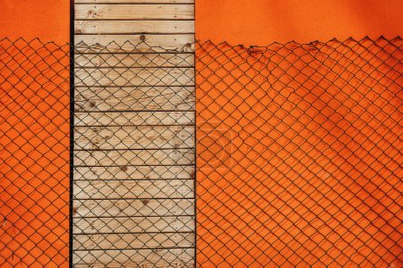 Téléchargez les photos : Chaîne lien clôture coulée ombre sur le mur orange et portes fermées avec des planches en bois, élément de conception - en image libre de droit