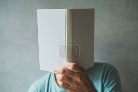 Foto de Lector masculino escondiendo su cara detrás del libro de maquetas blanco, enfoque selectivo - Imagen libre de derechos