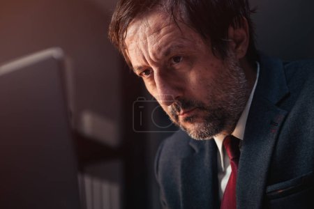 Foto de Retrato de primer plano de una persona de negocios caucásica cansada mirando la pantalla de la computadora portátil mientras trabaja hasta tarde en la oficina corporativa, enfoque selectivo - Imagen libre de derechos