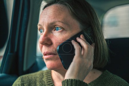 Retrato de mujer adulta madura infeliz grave durante la conversación telefónica en el asiento trasero del automóvil, enfoque selectivo