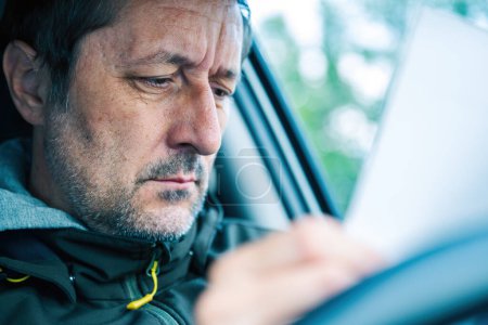Male driver reading paper document in the car, selective focus