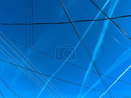Pattern of airplane contrails and electrical wires over blue sky in spring as background