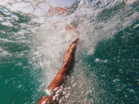 Hombre ahogándose en el mar azul profundo, cerca de la mano alcanzando la superficie del océano, rodeado de burbujas de aire, nadador luchando por su vida, enfoque selectivo