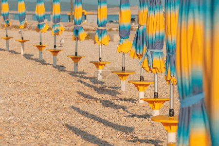 Téléchargez les photos : Parasols de plage pliés et colorés sur la côte de la mer Adriatique en été ensoleillé matin, vacances et arrière-plan de vacances avec espace de copie - en image libre de droit