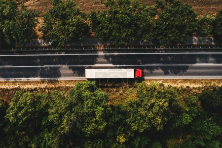 Téléchargez les photos : Concept de camionnage et de transport de marchandises, vue aérienne du semi-camion rouge avec remorque blanche sur route, directement au-dessus - en image libre de droit