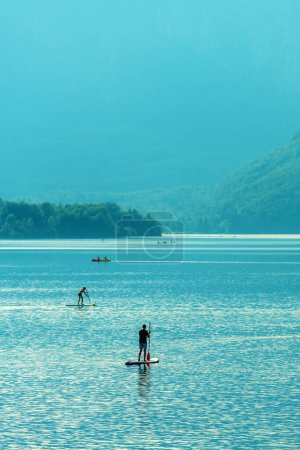 Téléchargez les photos : Activités nautiques sur le lac Bohinj en été, les gens ramant bateaux et pagayant sur des planches de stand-up, accent sélectif - en image libre de droit