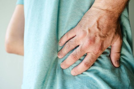 Foto de Síntomas de dolor de espalda, primer plano de la mano masculina sosteniendo el deporte doloroso en el lomo inferior de la espalda, enfoque selectivo - Imagen libre de derechos