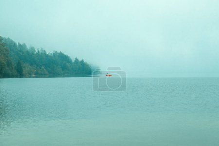 Téléchargez les photos : Deux personnes méconnaissables sur le canot orange ramant sur le lac Bohinj dans la matinée brumeuse, foyer sélectif - en image libre de droit