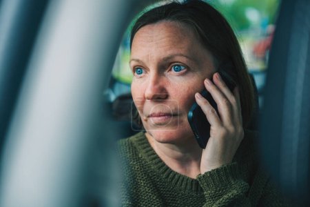 Photo for Portrait of serious disappointed mature adult female during phone call conversation at the back seat of the car, selective focus - Royalty Free Image