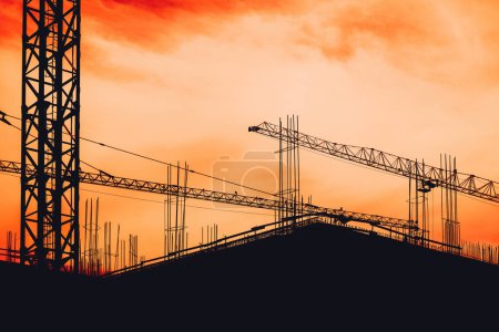 Téléchargez les photos : Chantier de construction échafaudage et grues en silhouette contre le spectaculaire coucher de soleil orange - en image libre de droit