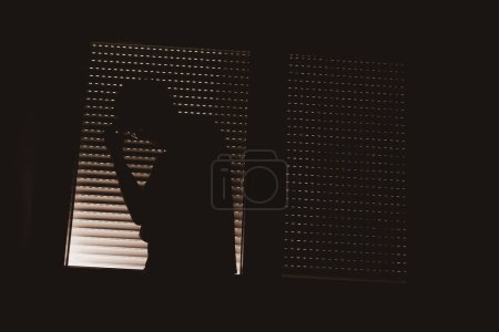 Concept de trouble de la personnalité paranoïaque, silhouette d'homme par la fenêtre avec volets fermés, discret