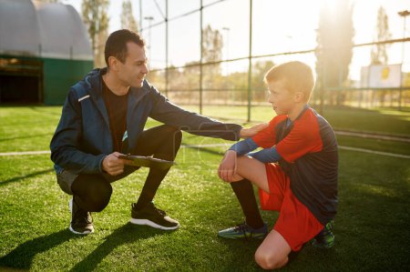 Young soccer coach giving support and advice to sad worry little football player. Coach talking putting hand on kid shoulder