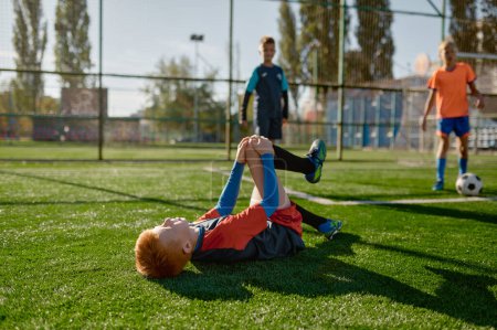 Photo for Young boy soccer player with injured knee lying on field during match. Hurt kid footballer with painful leg on ground in agony having bad day on pitch - Royalty Free Image