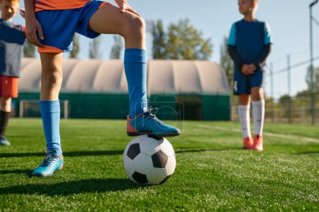 Photo for Young soccer player holding boots on ball cropped shot. Kids team practicing soccer on grass venue - Royalty Free Image