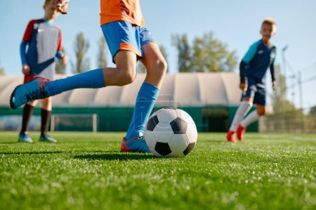 Photo for Closeup boy kicking ball while playing football with teammates on outdoor grass field. Soccer tournament for children - Royalty Free Image