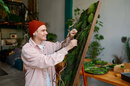 Foto de Joven diseñador creando composición floral en el estudio de arte. Floristería hipster calificada trabajando en taller - Imagen libre de derechos