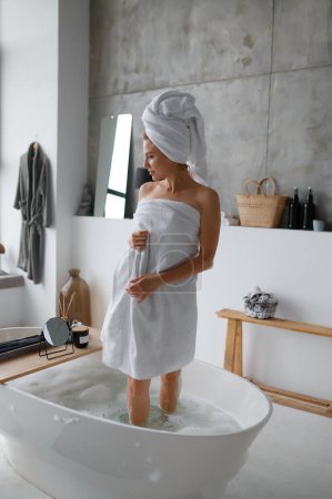 Foto de Mujer joven con toalla blanca en la cabeza y el cuerpo saliendo del baño. Cuidado del cuerpo de la mañana, cuidado de la piel en el concepto de baño - Imagen libre de derechos