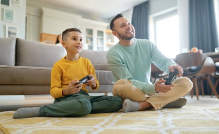 Téléchargez les photos : Heureux père et fils jouant jeu vidéo assis sur le sol de la maison salon. Parent et enfant passent du temps ensemble - en image libre de droit