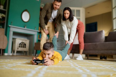 Photo for Parents struggle with child addicted to video game. Mother and father holding and pulling boy leg trying to get him out. Internet, digital gadget and technology addiction - Royalty Free Image