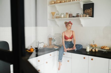 Téléchargez les photos : Young woman in lingerie with bottle of milk sitting on kitchen table - en image libre de droit