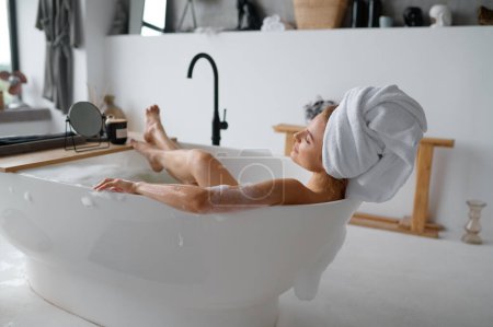 Téléchargez les photos : Vue aérienne sur jeune femme adulte couchée dans le bain avec bulle de mousse de savon relaxant à la maison le week-end - en image libre de droit
