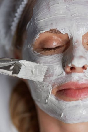 Téléchargez les photos : Closeup top view on cosmetologist brush applying clay mask on female client face - en image libre de droit