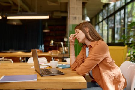 Foto de Tired young business woman relaxing and stretching exercise on neck and shoulders while working at coworking space - Imagen libre de derechos