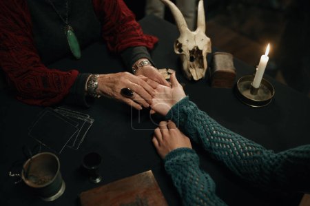 Photo for Top view on fortune teller and client hands over table with spiritual attributes as candle, wild animal skull. Prediction future and palmistry concept - Royalty Free Image