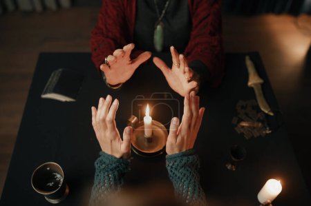 Téléchargez les photos : Clairvoyant and client holding hand over candle flame top view. Mystery and spirituality concept - en image libre de droit