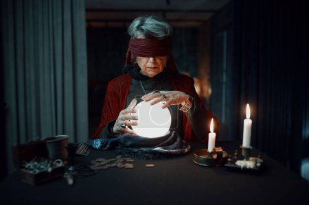 Photo for Blindfolded fortune teller medium using glowing crystal ball for future reading. Online spiritual session and divination concept - Royalty Free Image