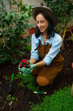 Foto de Portrait of attractive young woman florist showing beautiful flowerpot to camera. Garden greenhouse work concept - Imagen libre de derechos
