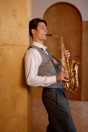 Photo for Jazz musician playing saxophone and leaning against art studio wall. Practicing before performance - Royalty Free Image