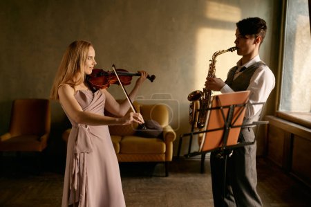 Téléchargez les photos : Young female violinist and male saxophonist training at home studio before music concert performance - en image libre de droit