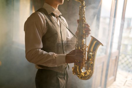 Téléchargez les photos : Young male saxophone player foggy toned cropped shot. Jazz band saxophonist practicing at home - en image libre de droit