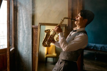 Photo for Young elegant man playing gold alto saxophone in misty room. Emotional musician with sax - Royalty Free Image