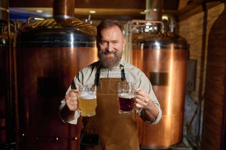 Photo for Satisfied senior brewer posing for camera with pale ale and dark beer pint in hand. Portrait of successful brewery owner advertising freshly made craft drink with different flavor - Royalty Free Image