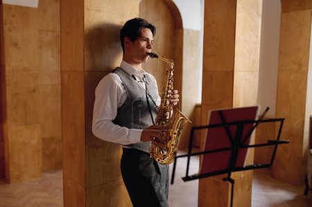 Téléchargez les photos : Jazz musician playing saxophone and leaning against art studio wall. Training before performance - en image libre de droit