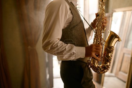 Téléchargez les photos : Cropped shot of unrecognizable male musician playing his saxophone at home. Making music with air - en image libre de droit