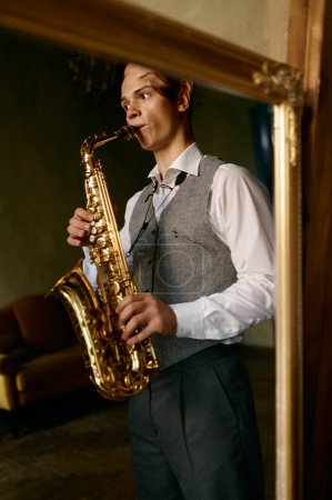 Photo for Young man playing saxophone in reflection of mirror at home. In love with music - Royalty Free Image