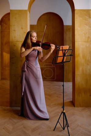 Foto de Lonely young female violinist playing fiddle at studio. Full-length portrait of musician - Imagen libre de derechos