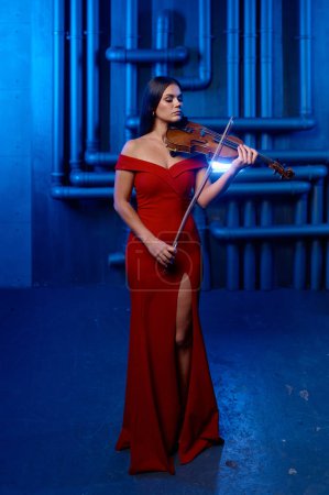 Photo for Young pretty woman playing violin solo over loft interior background. Musician playing classical music on musical instrument - Royalty Free Image