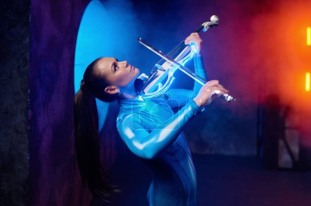 Photo for Emotional pretty woman artist playing violin in neon light and haze over loft industrial studio background - Royalty Free Image